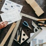 Tools and hands on a workbench during a woodworking project featuring plans and equipment.