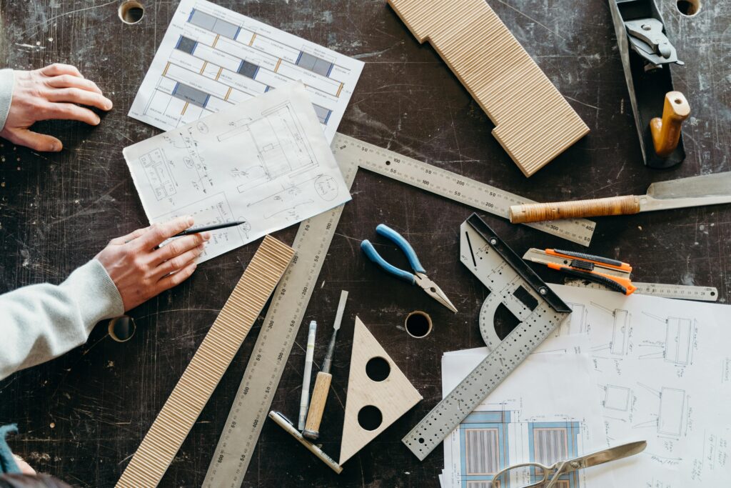 Tools and hands on a workbench during a woodworking project featuring plans and equipment.